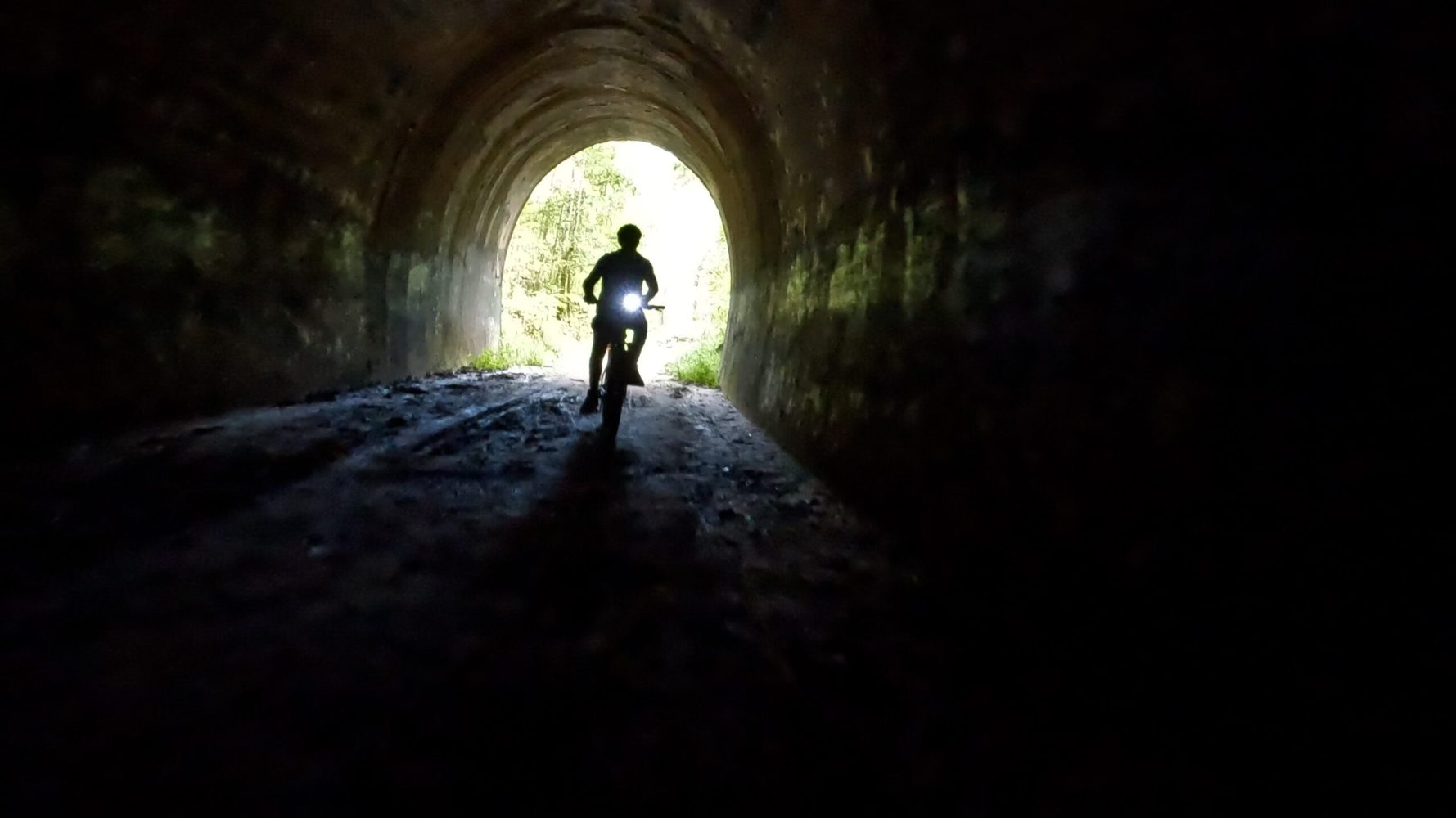 Silhouetted e-MTB rider entering the Dularcha Railway Tunnel, with the northern arch entrance illuminated by background light.